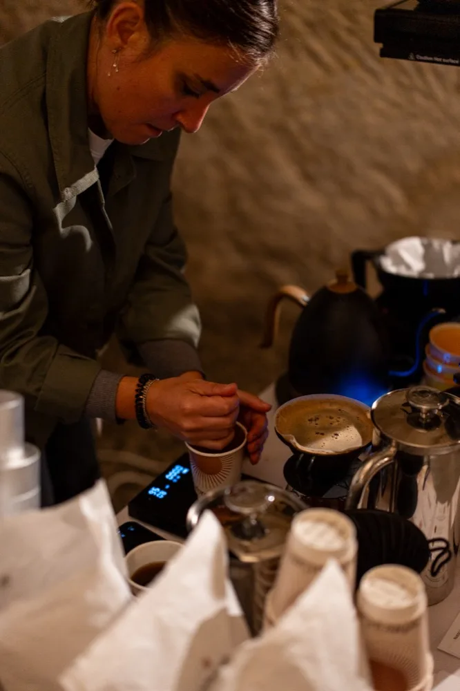 Une barista prépare un café filtre sur un stand du festival, devant un mur de pierre